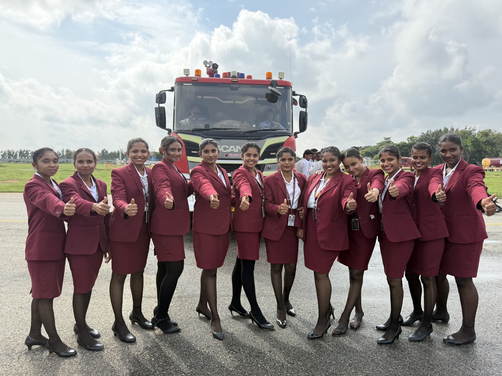 Twelve cabin crew trainees giving a thumbs up in front of an Airport fire and rescue truck