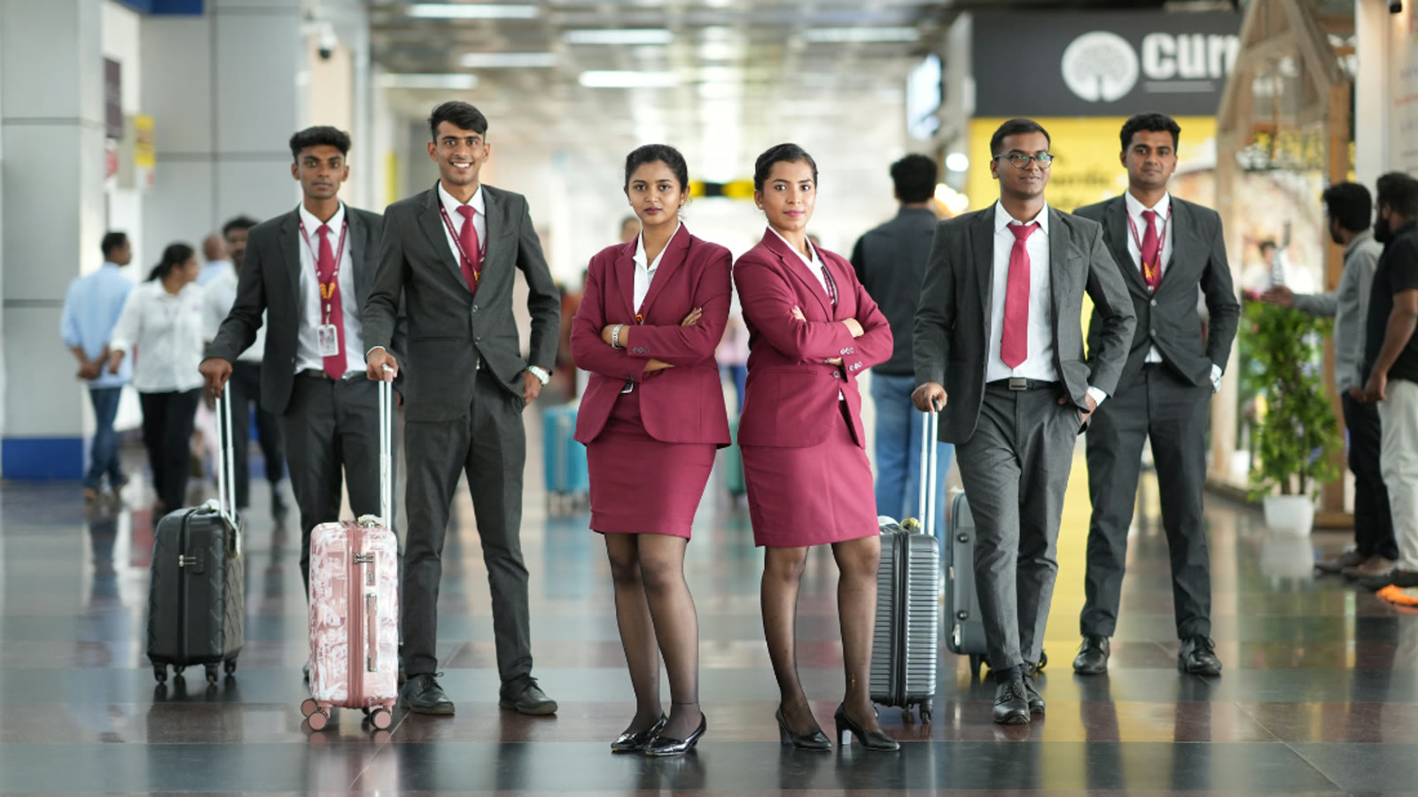 Six Brandcrew students in cabin crew and ground staff uniform standing with their luggage in an Airport terminal